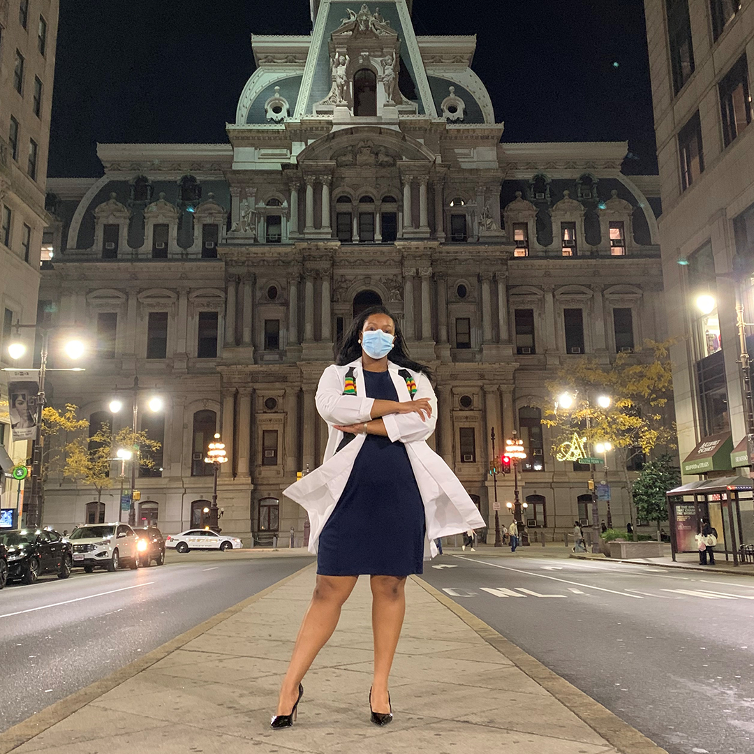 Lena Ward stands in PA white coat and graduation stole in front of Philadelphia's City Hall